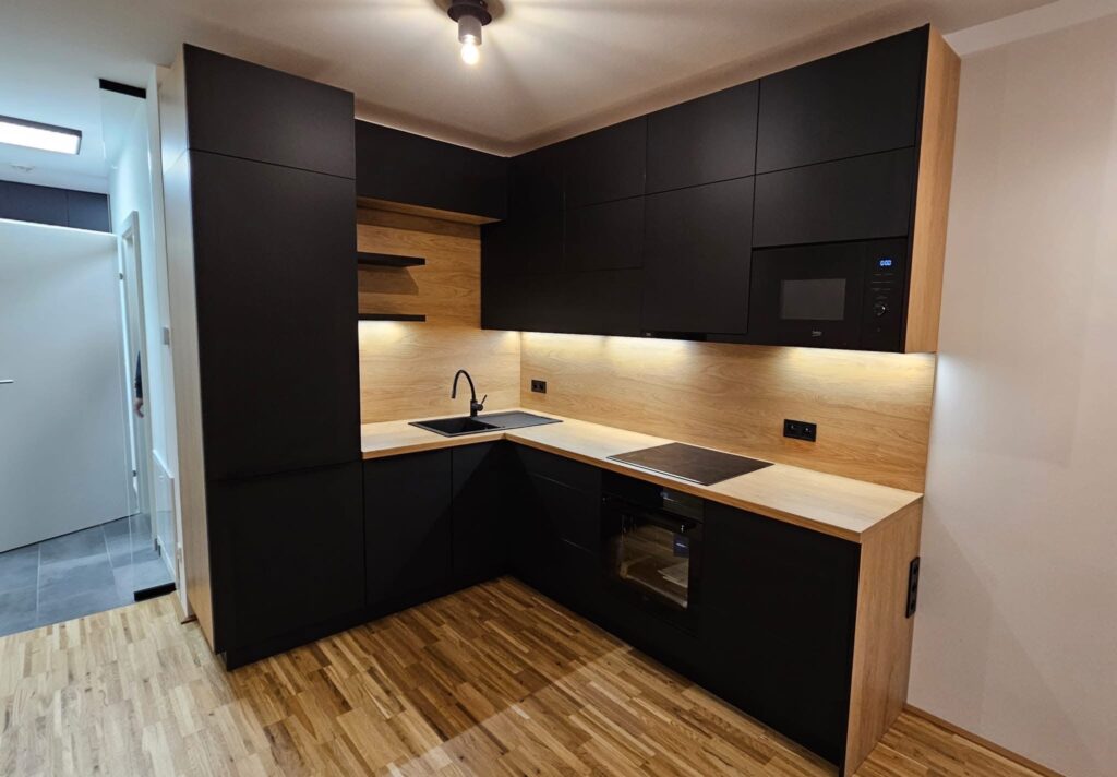 Moderní černá kuchyně s světlým dekorem dřeva.